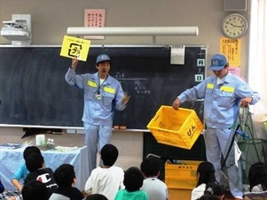 写真：資源の分け方と出し方を説明する清掃職員と、説明を聴く児童