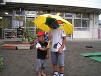 写真：突然の雨で年長児が傘をさしかけてあげています
