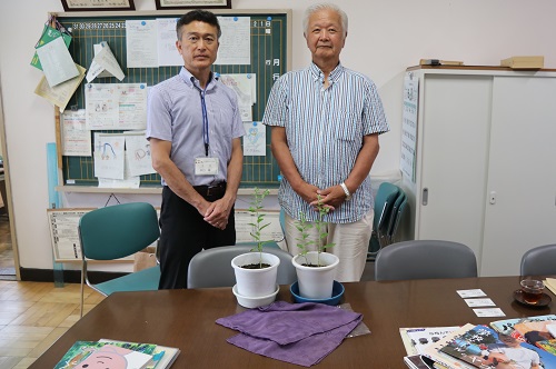 校長と竹下さんが寄贈されたムラサキの前に並ぶ写真