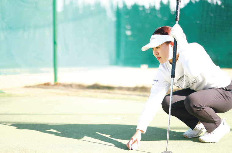 クラブとボールを持ち、芝生にしゃがんで先を見つめる小俣さんの画像